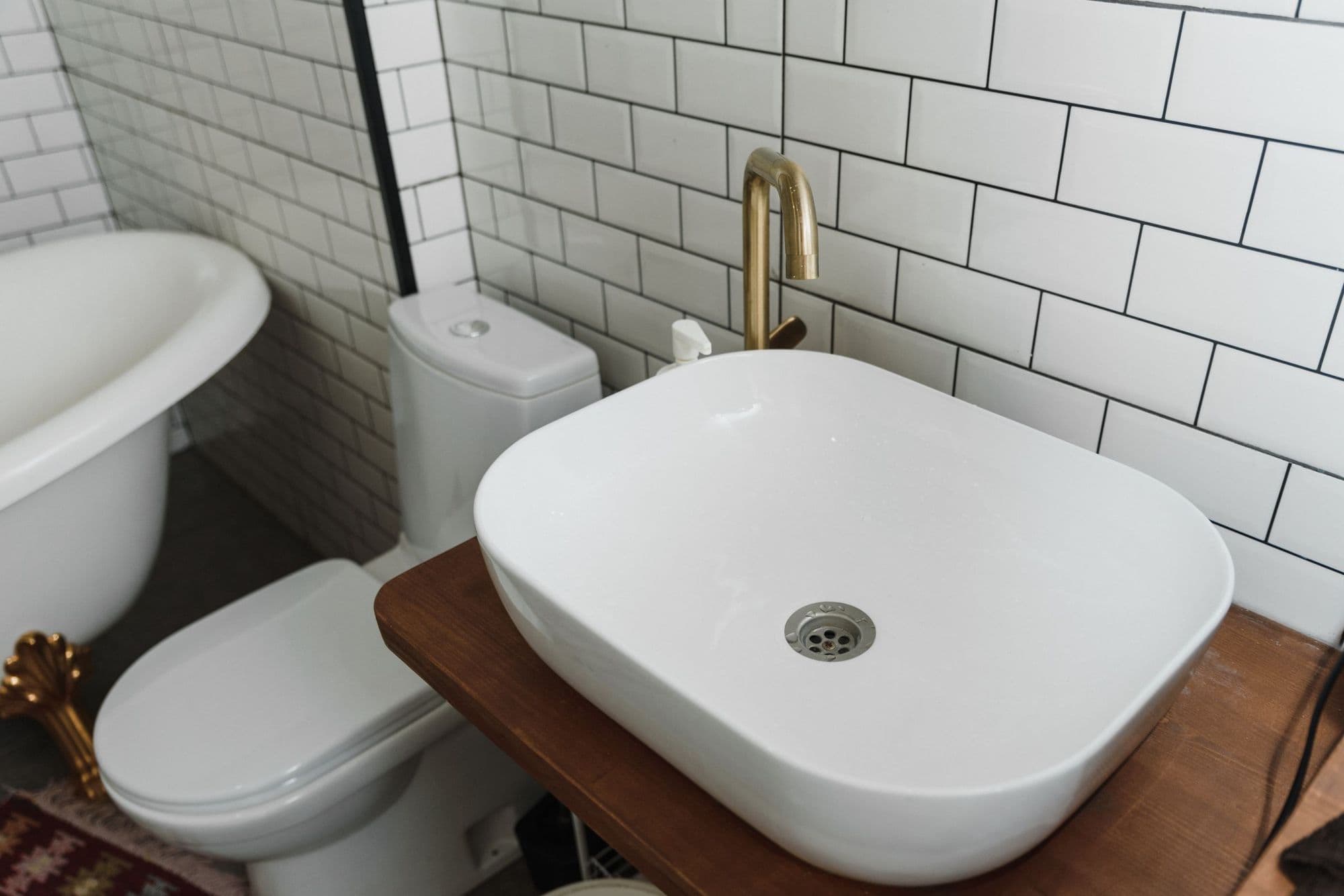 Fehér pultra ültetett mosdó fapolcon, mögötte WC és metrócsempe